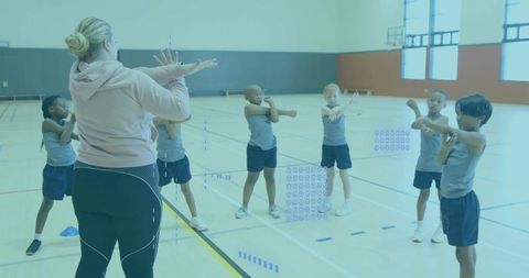 School PE instructor leading dynamic warm-up stretches with children in bright gymnasium