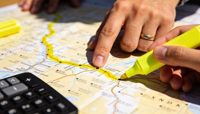 Couple planning road trip tracing route on map with yellow highlighter and calculator