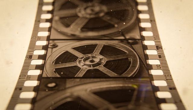 Displaying backlit vintage film strip with movie reels and sprocket holes in sepia macro