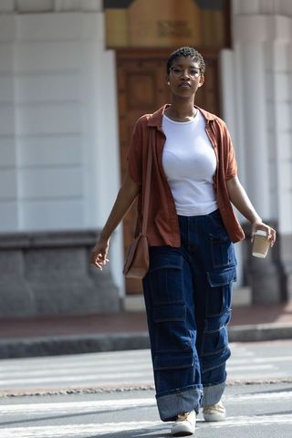 African woman walking across zebra crossing holding coffee and tan crossbody bag city style