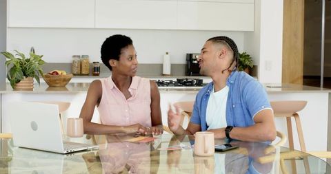 Couple discussing budget while reviewing laptop and phone at modern kitchen table