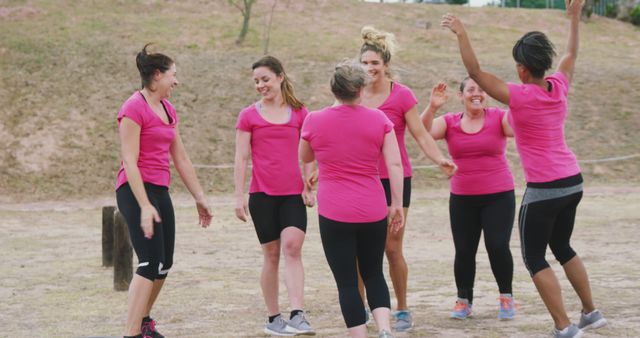 Group of women wearing pink shirts participating in team bonding activities outdoors. They appear happy and energetic as they engage in a fun exercise session. Ideal for themes related to teamwork, fitness, women's health, friendship, and active lifestyles.