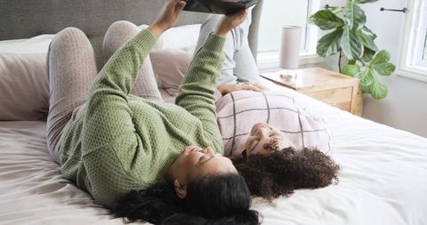Mother and daughter lying on bed sharing tablet, cozy family bonding in sunlit bedroom