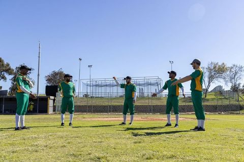 Cricket team warming up on grassy field in green and yellow uniforms under clear sky