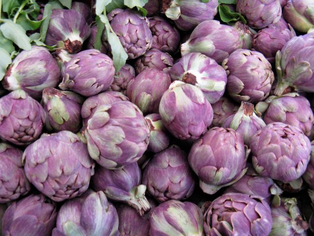 Closeup view of vibrant purple artichokes at farmers market. Ideal for use in content promoting healthy eating, organic farming, or culinary themes. Useful for blog posts, recipe articles, food market promotions, or vegetable gardening content.