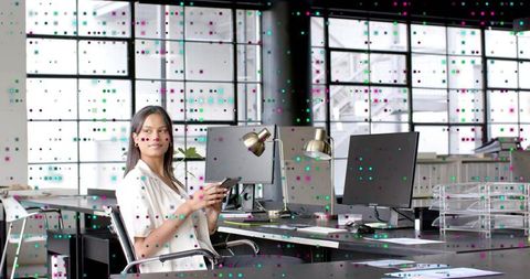 Young professional holding smartphone in modern open-plan office with digital data overlay