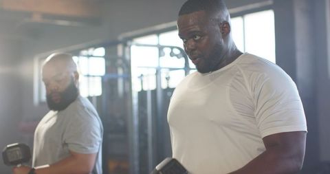 African men lifting heavy dumbbells together in gym showing strength and focus
