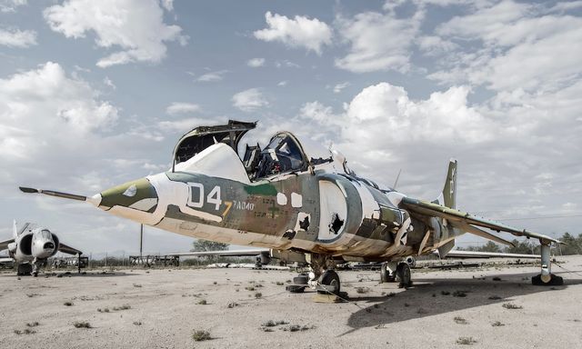 Abandoned military fighter jet in decay on an old airfield, showcasing rusting camouflage paint, broken parts. Uses: historical documentaries, military history articles, vintage aviation features, educational content on obsolete technology.