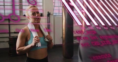 Woman catching breath after workout, gym glass showing pink data overlay