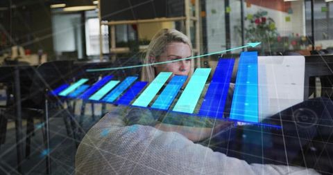 Woman analyzing data on laptop with blue holographic bar chart in coworking office