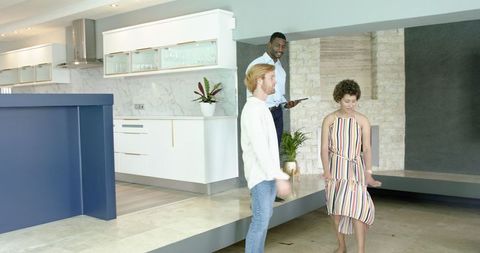 Diverse Couple Touring Modern Home With Realtor Using Tablet