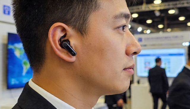 Asian businessman listening with wireless earbud at tech expo, networking, connectivity