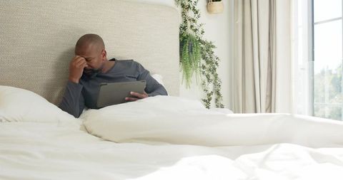 Man reflecting with digital tablet in calm bedroom setting