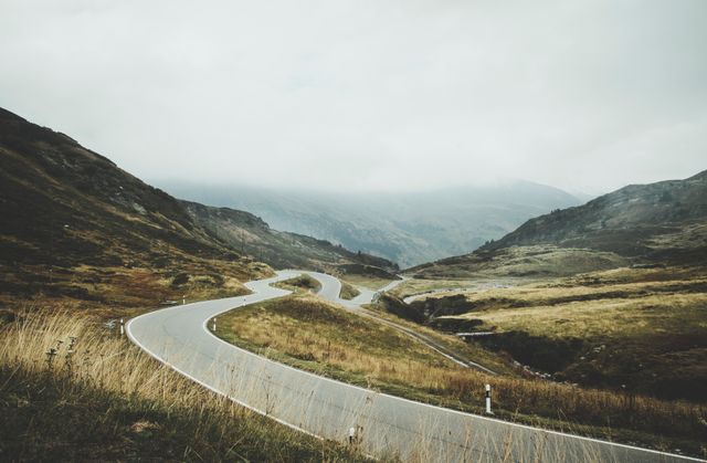 Winding road through mountain landscape on cloudy day captures the serene beauty of nature. This can be used for travel blogs, nature journeys, scenic route promotions, and adventure storytelling.