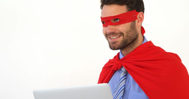 A Caucasian man dressed in business attire with a superhero cape and mask holds a laptop, with copy space. His playful costume suggests a fun approach to work or the concept of tackling challenges with a superhero mindset.