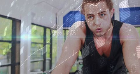 Focused young man pedaling on stationary bike with digital HUD overlay, sunlit gym training