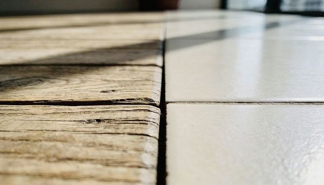 Close-up rustic wood to ceramic tile floor transition showing weathered grain, seam, light