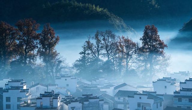 Misty autumn village nestling in forest valley with white-walled houses and tiled roofs