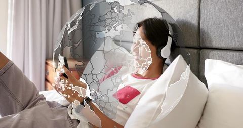 Teen relaxing on bed listening to music and browsing smartphone with global overlay