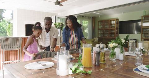 Black family arranging sunlit outdoor dining table with floral garland and candles