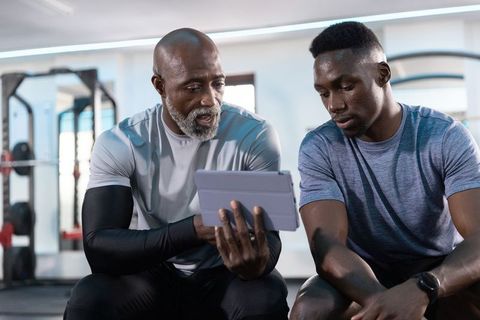 African american personal trainer coaching young athlete using tablet in modern gym
