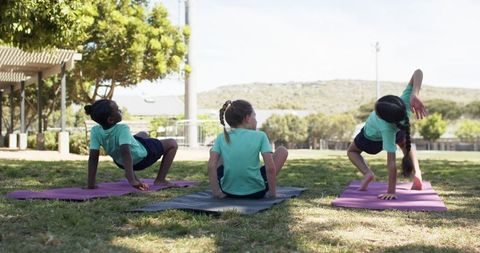 Girls Practicing Yoga and Stretching Together on Sunlit Park Lawn Wearing Matching Teal Shirts
