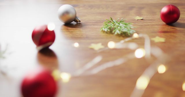 Soft focus image showing Christmas decorations on a wooden table. Red and silver ornaments are placed alongside small sprigs of greenery and golden star-shaped confetti. Warm fairy lights create a cozy seasonal atmosphere with a bokeh effect. Ideal for use in holiday-themed designs, festive social media posts, or as a background for Christmas promotions.