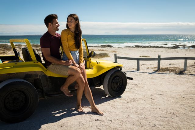 Couple enjoying a romantic moment sitting on a yellow beach buggy by the sea. Ideal for use in travel advertisements, romantic getaway promotions, summer holiday campaigns, and lifestyle blogs. Perfect for conveying themes of love, adventure, and carefree summer fun.