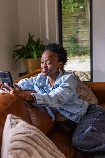 African american woman reclining on sofa smiling using smartphone in modern living room