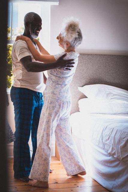 Diverse senior couple having fun dancing together in bedroom smiling. staying at home in isolation during quarantine lockdown.