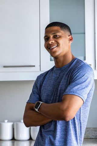 Confident african american man standing in kitchen wearing smartwatch and blue tee