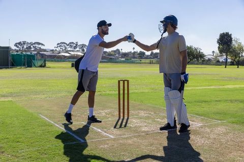 Cricket teamwork: batsman and teammate exchanging glove tap at crease before practice