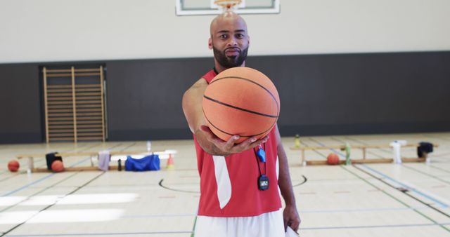 Portrait of happy african american male basketball coach holding ball on indoor court. Sport, fitness, health and team sport, unaltered.