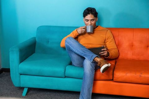 Man sipping coffee while using tablet on vibrant two-tone teal and orange sofa