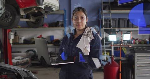 Latina mechanic holding laptop diagnosing car in modern garage with work lights and tools