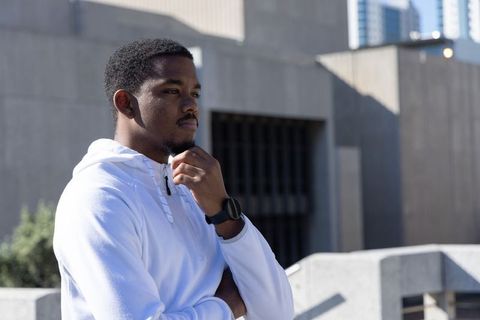 Young african american man contemplating on urban rooftop wearing white hoodie and smartwatch