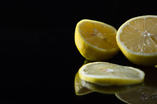 This image features a close-up of a fresh lemon sliced open, set against a black background. The vibrant yellow color of the lemon contrasts sharply with the dark background, highlighting its freshness and juiciness. Ideal for use in food blogs, health and wellness articles, advertisements for citrus products, or any content related to healthy eating and nutrition.