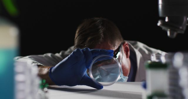 Caucasian male doctor wearing face mask and gloves inspecting petri dish. healthcare, medical research and hygiene during coronavirus covid 19 pandemic.