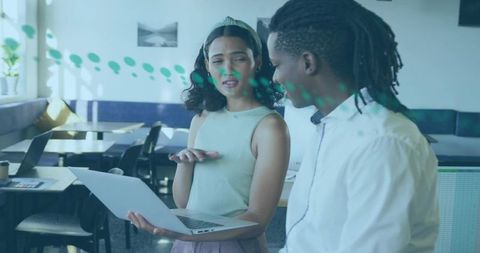 Young professionals collaborating over laptop in bright coworking cafe with green accents