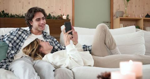 Couple Relaxing on Sofa with Smartphone in Warm Living Room