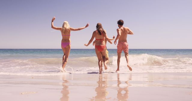 Three young Caucasian individuals are enjoying a sunny day at the beach, running towards the ocean waves, with copy space. Their carefree attitude and the clear blue sky create a sense of summer joy and freedom.