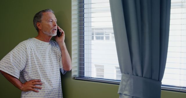 Senior Man in Hospital Gown Talking on Phone by Window - Download Free Stock Images Pikwizard.com