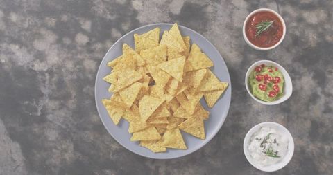 Blue plate stacked with tortilla chips and trio of salsa guacamole sour cream dips flatlay