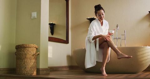 Biracial woman with vitiligo applying body lotion in relaxing bathroom