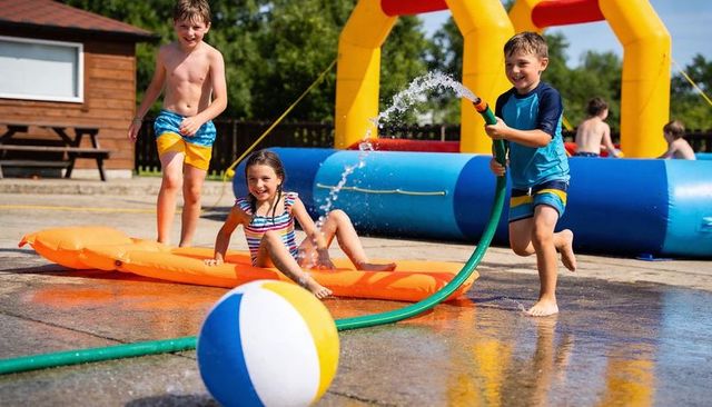 Kids splashing with water hose at summer camp inflatable pool play with beach ball