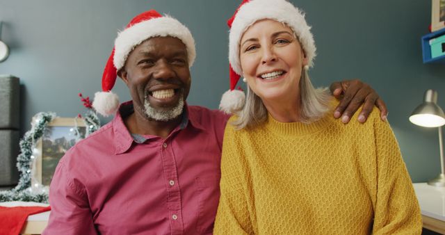Older couple wearing Santa hats, smiling and embracing, celebrating Christmas at home. Ideal for holiday marketing, greeting cards, family-oriented promotions, and festive advertisements appealing to togetherness and happiness.
