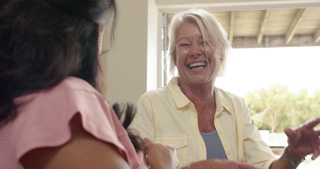 Senior woman smiling and talking with friend outdoors, showcasing friendship and happiness. Suitable for use in positive aging, friendship-focused, and social connection themes.