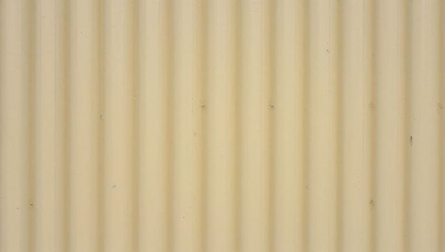 Corrugated beige metal siding featuring narrow ridges, scuffed texture and light rust