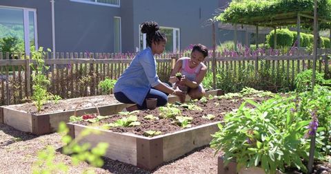 African mother teaching daughter gardening in backyard raised beds growing vegetables