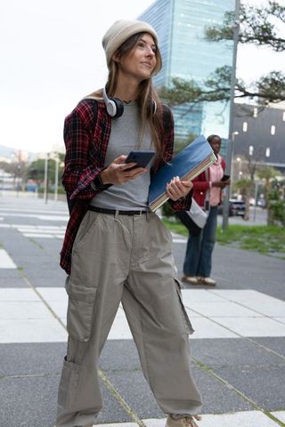Urban student walking holding smartphone and notebook wearing beanie and headphones on crosswalk